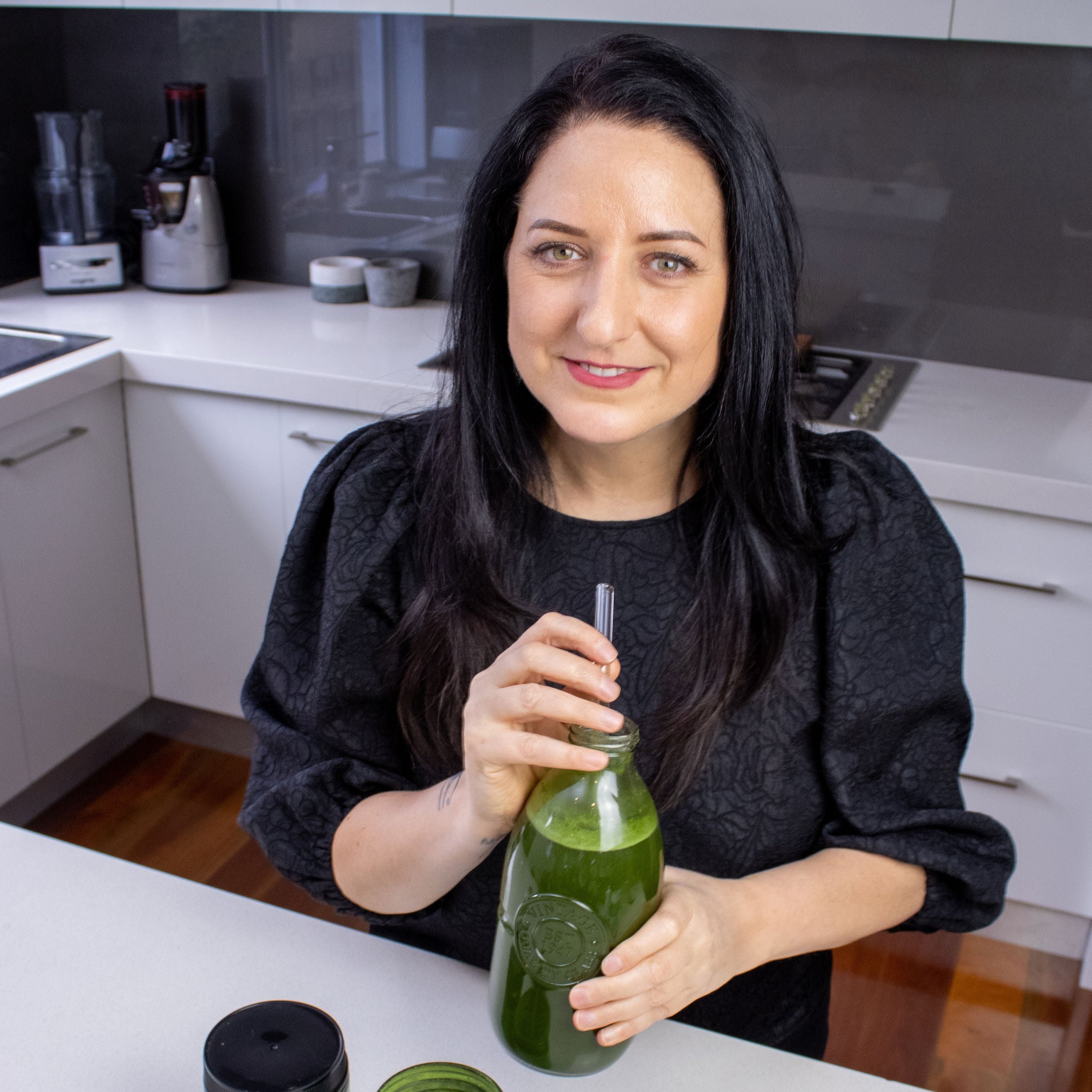 Diane Hackner holding a green smoothie in a kitchen with jars on the counter