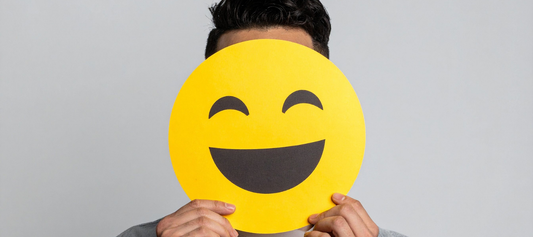 Man holding a smiley face mask in front of his face to represent toxic positivity and emotional suppression.