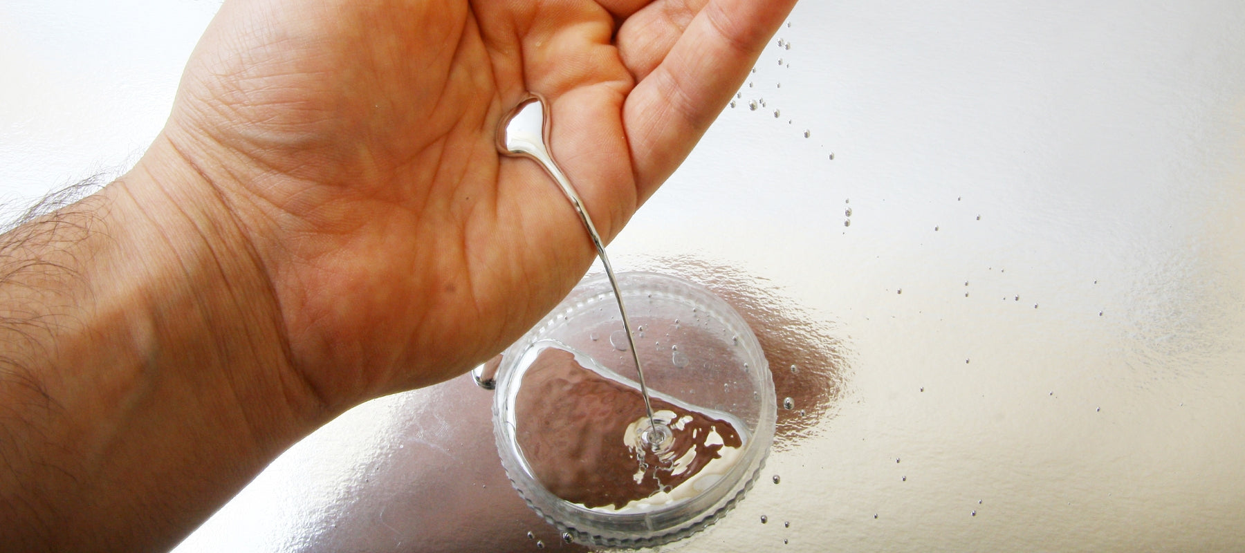 Hand pouring a Liquid Metal into a small container on a reflective surface.