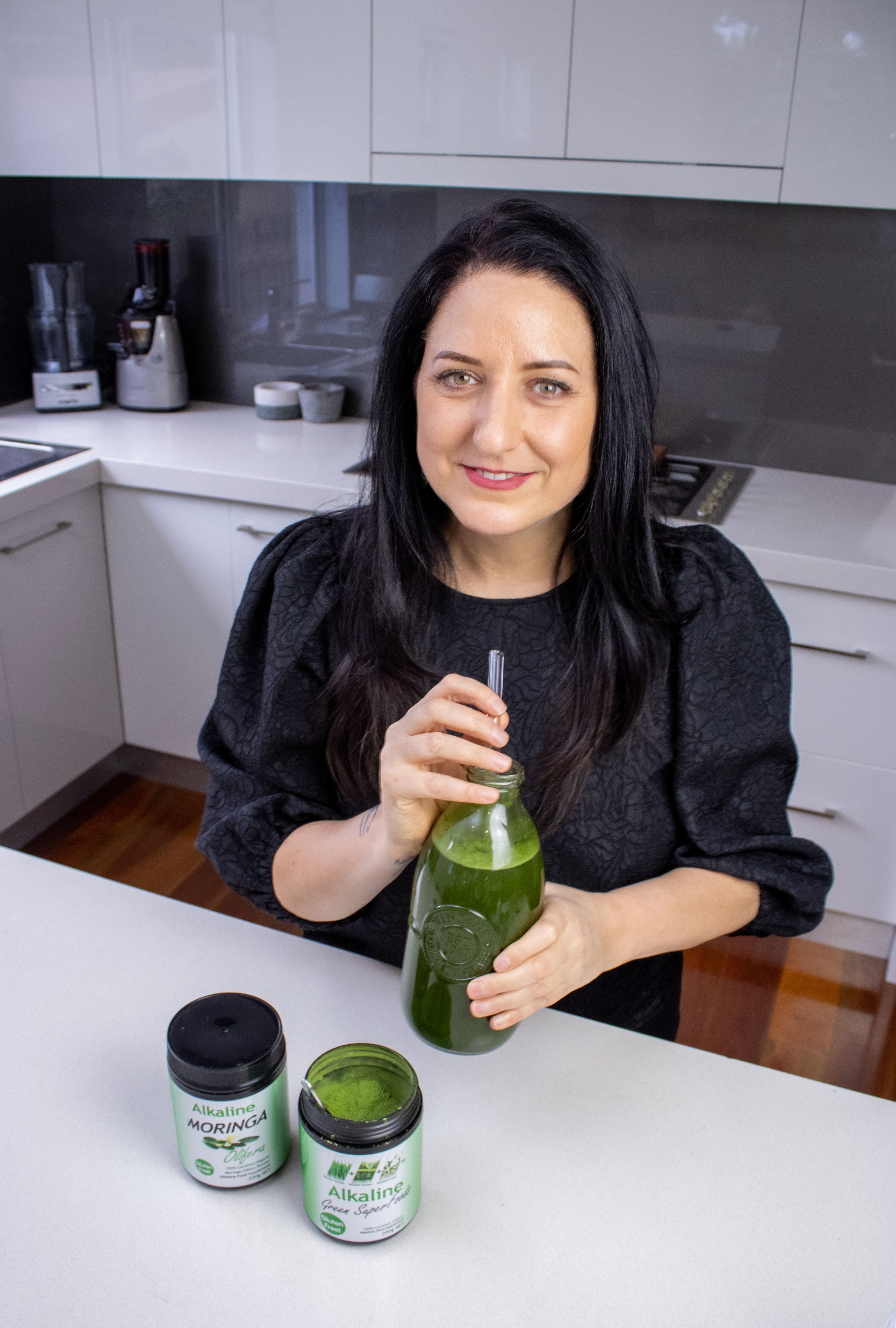 Diane Hackner holding a green superfood drink in her kitchen.