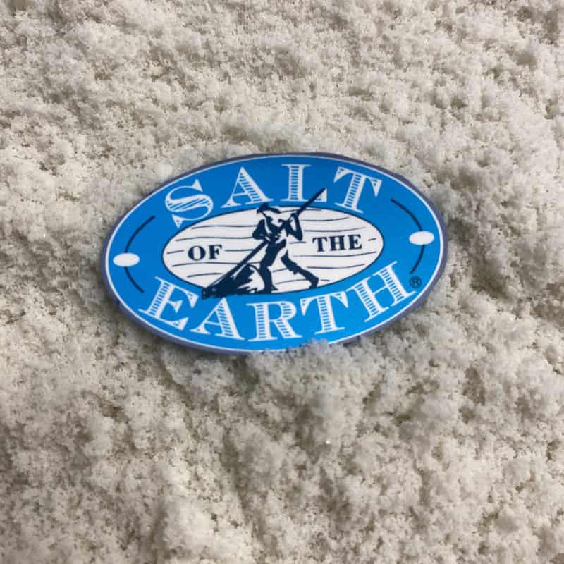 Loose Salt of the Earth Fine Celtic Sea Salt crystals with Salt of the Earth logo card on top – unrefined mineral-rich gourmet sea salt close-up.
