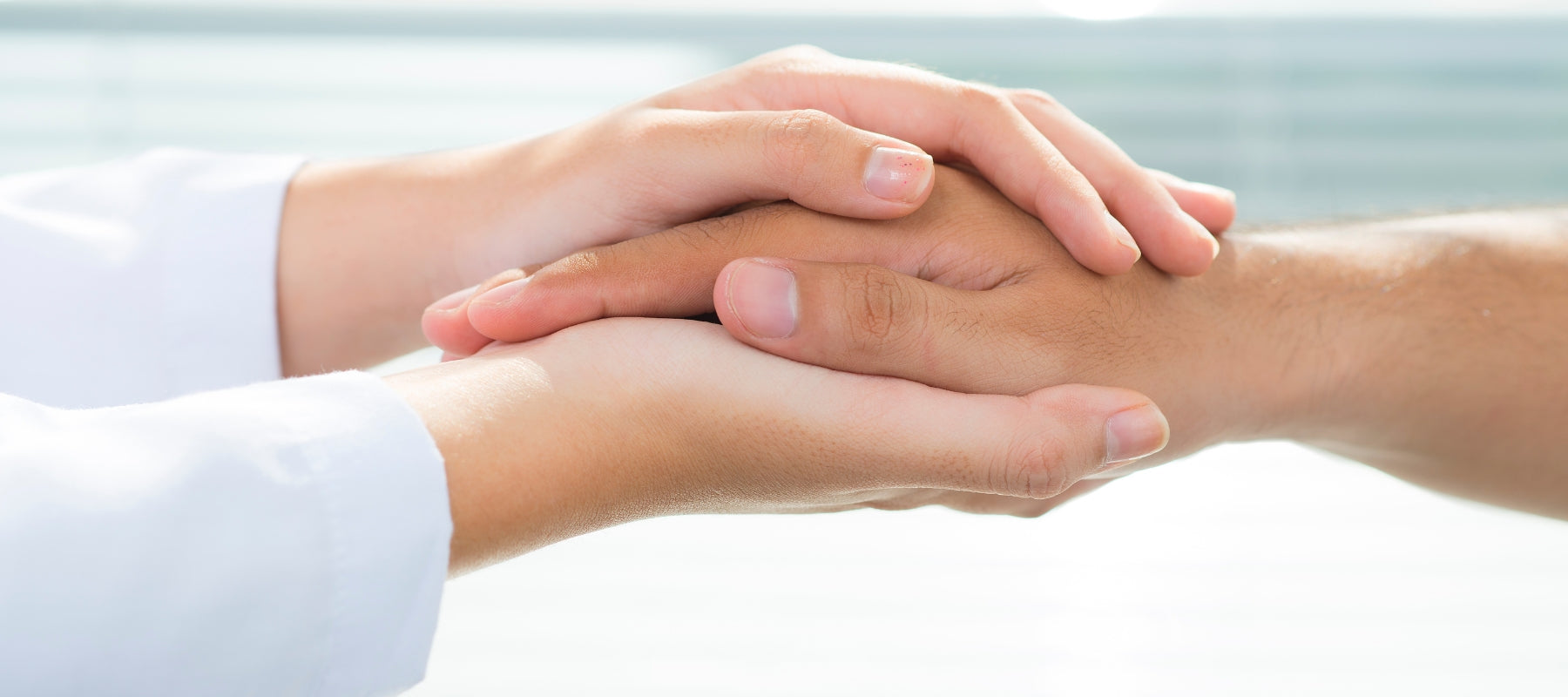 Two hands, one in a white sleeve, holding each other against a light background