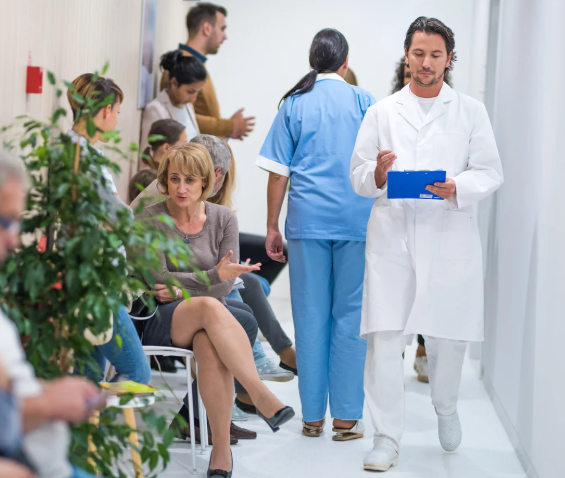 Doctor holding a tablet in a hospital setting with patients and staff.